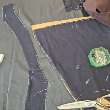Pezzi del cartamodello tagliati e spillati uno all'altro, con forbici da sarta e bottoni a pressione pronti sul tavolo